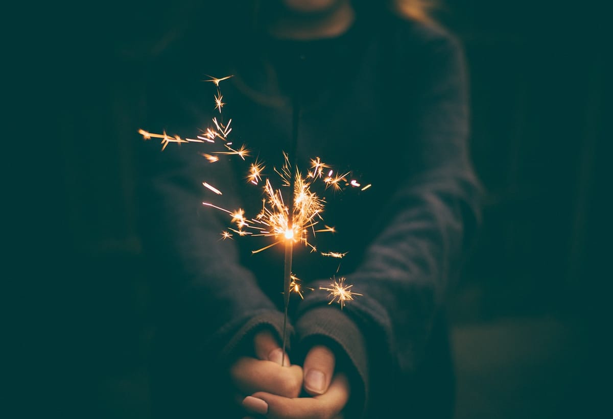 Person in shadow holds a sparkler in both hands.